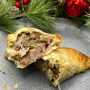 Golden baked Christmas pasty filled with turkey, stuffing, bacon, sausage, and cranberry sauce.